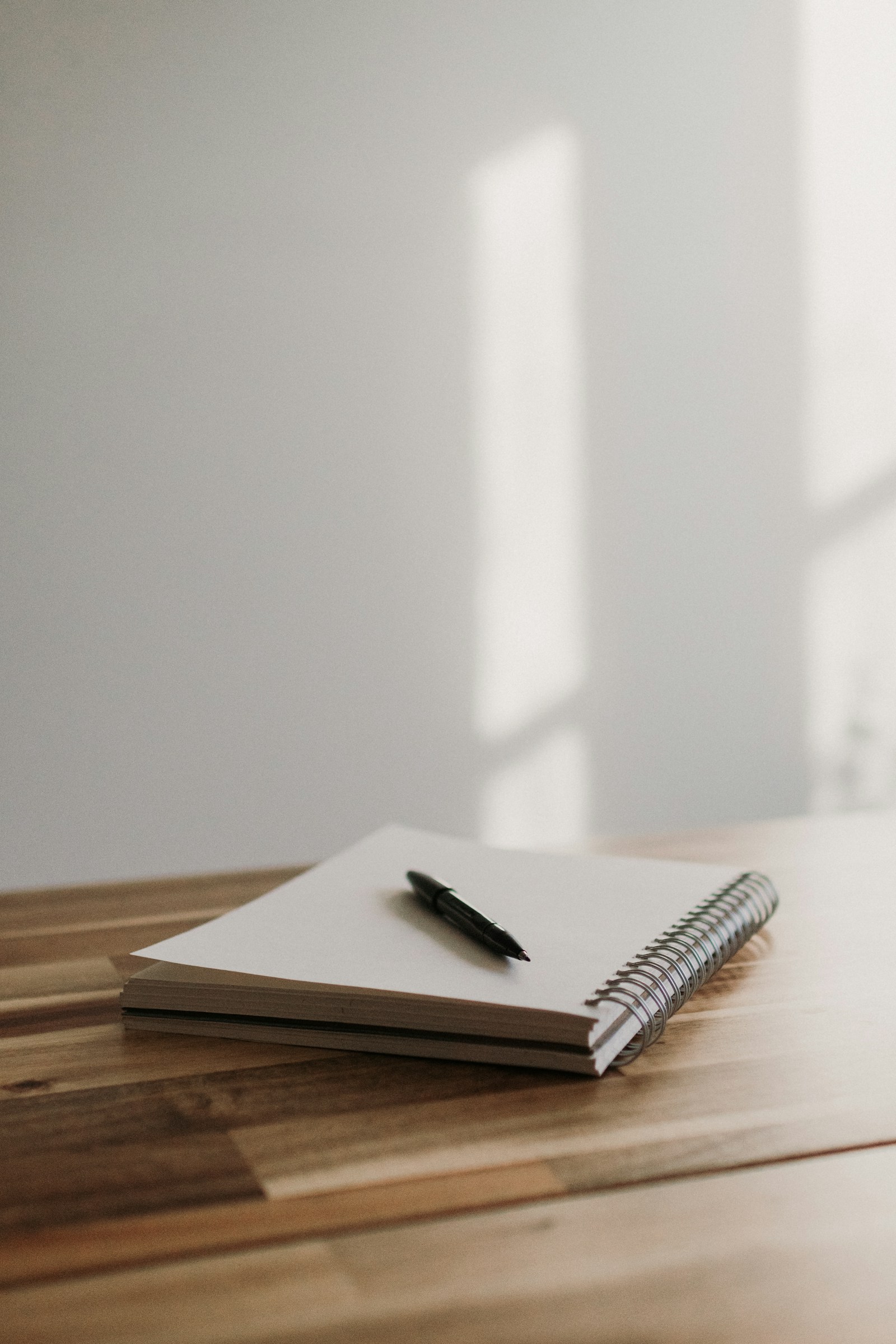 A notebook and pen on a wooden desk in soft natural window light